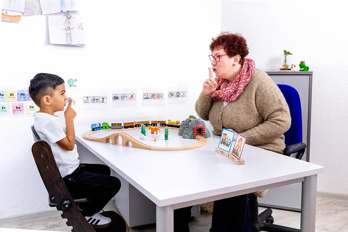 Sprachtherapie für Kinder in Dortmund: Therapeutin übt mit einem Jungen die Lautbildung am Therapietisch