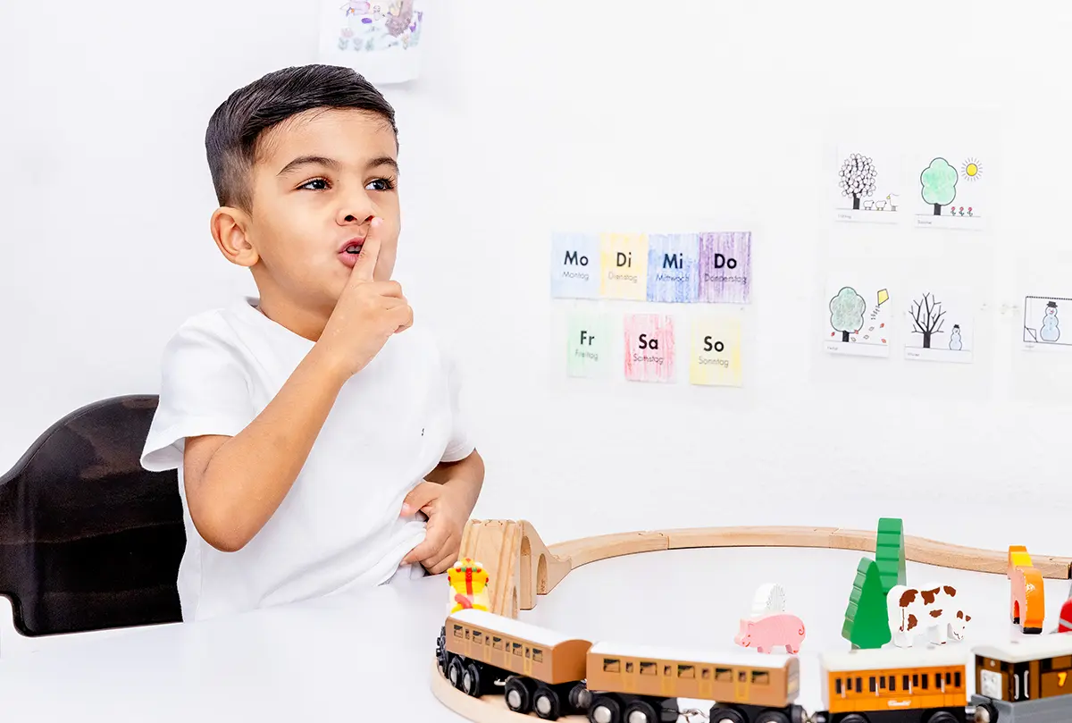 Junge übt in der Sprachtherapie einen Laut, im Hintergrund Silbenkarten an der Wand