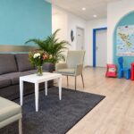Wartezimmer der Praxis für Sprachtherapie in Dortmund mit grauem Sofa, hellen Sesseln und Kinderspielecke